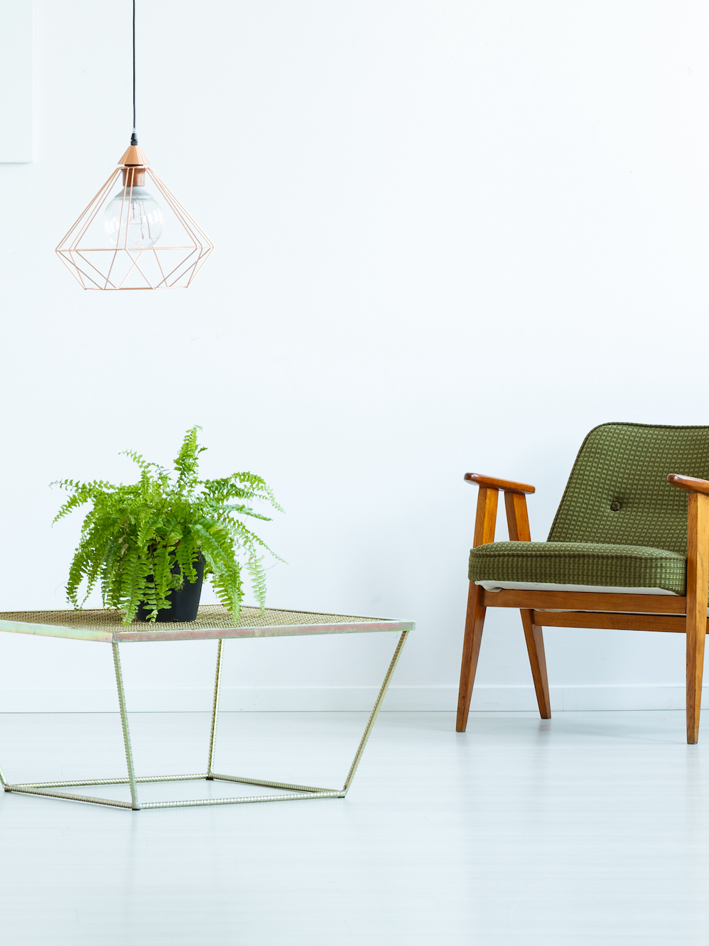 Table with plant between pouf and green armchair in white flat interior with yellow painting. Real photo